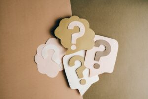 Gedankenblasen und Sprechblasen mit Fragezeichen auf einem Beige-Braunen Untergrund